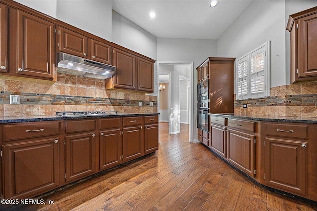 kitchen with under cabinet range hood, backsplash, dark wood-style flooring, dark stone counters, and recessed lighting
