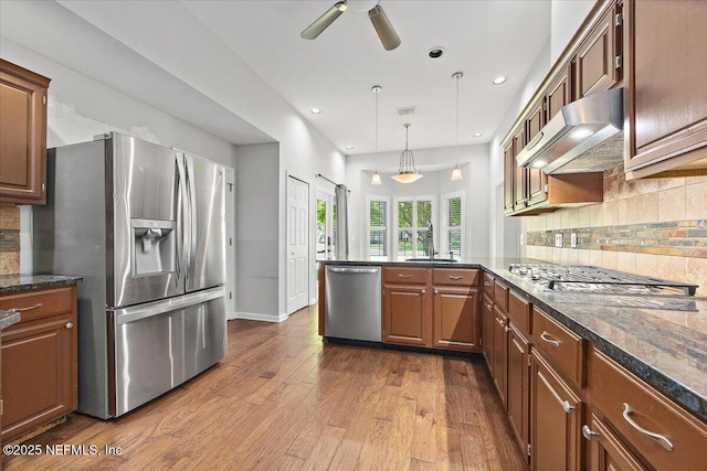 kitchen featuring stainless steel appliances, under cabinet range hood, a sink, a ceiling fan, and a peninsula