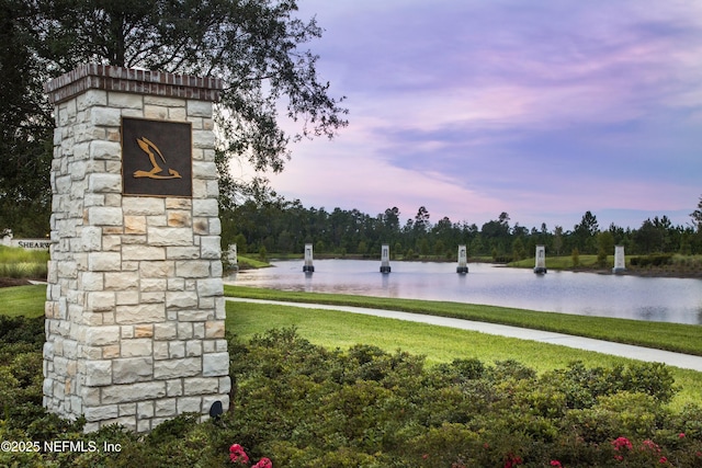 community / neighborhood sign featuring a water view, a lawn, and view of scattered trees