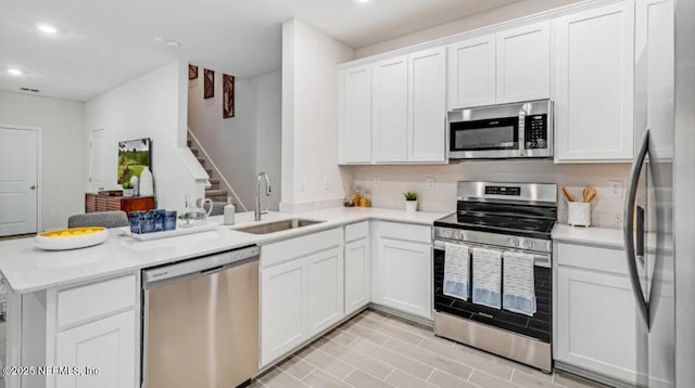 kitchen featuring stainless steel appliances, a sink, a peninsula, recessed lighting, and light countertops