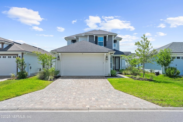 traditional-style house featuring a front yard, an attached garage, a shingled roof, and decorative driveway
