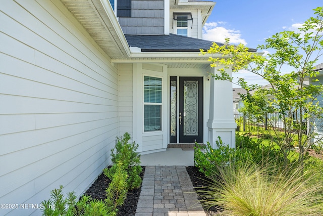 entrance to property featuring fence and roof with shingles