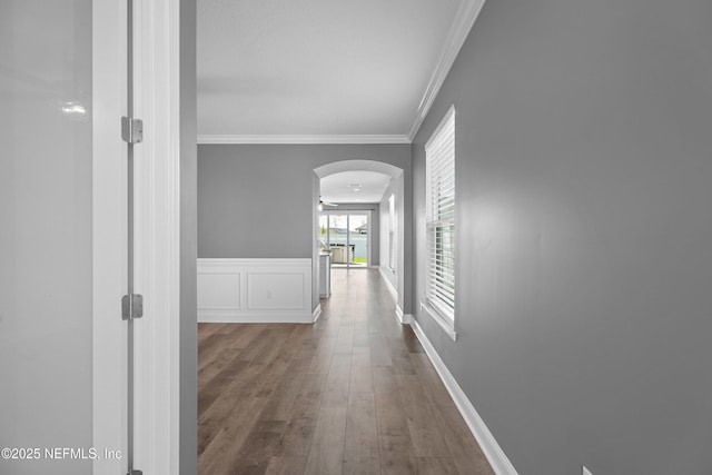 hallway with arched walkways, wood finished floors, crown molding, and wainscoting