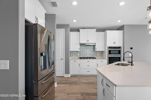 kitchen featuring appliances with stainless steel finishes, a sink, under cabinet range hood, light wood-style floors, and white cabinetry