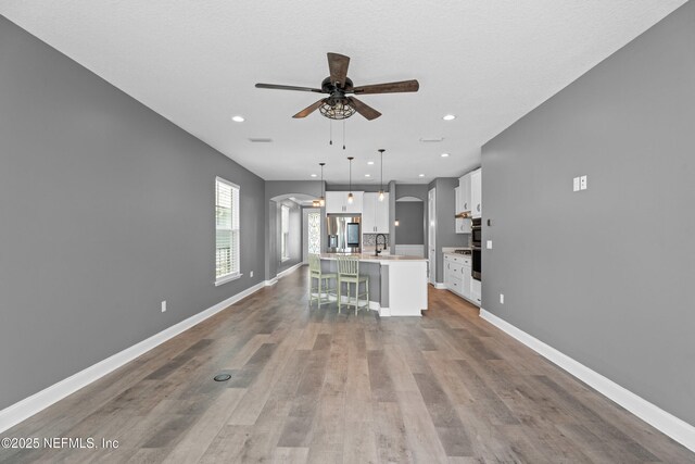 unfurnished living room featuring arched walkways, ceiling fan, wood finished floors, recessed lighting, and baseboards