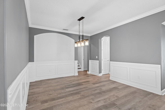 unfurnished dining area featuring arched walkways, ornamental molding, wood finished floors, a wainscoted wall, and a decorative wall