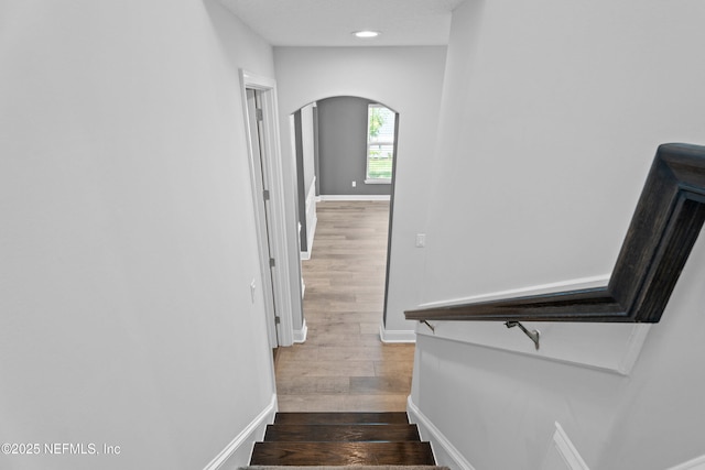 stairway with arched walkways, wood finished floors, baseboards, and recessed lighting