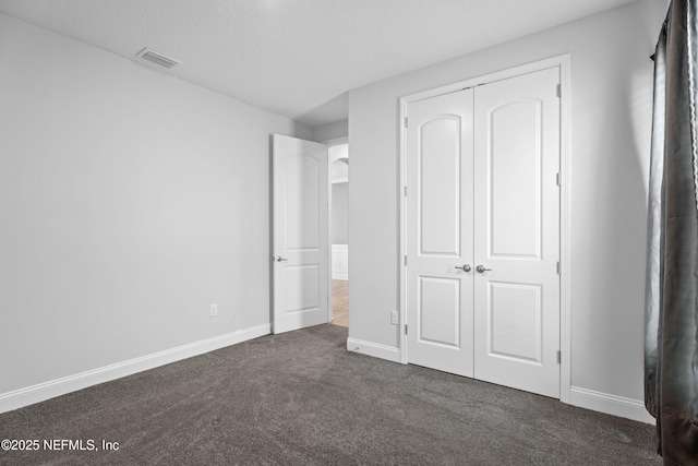 unfurnished bedroom with dark carpet, baseboards, and a closet