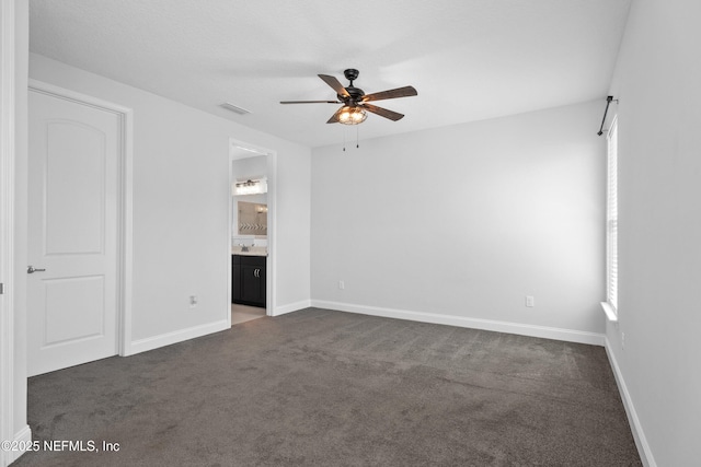 unfurnished bedroom featuring dark colored carpet, baseboards, connected bathroom, and a ceiling fan