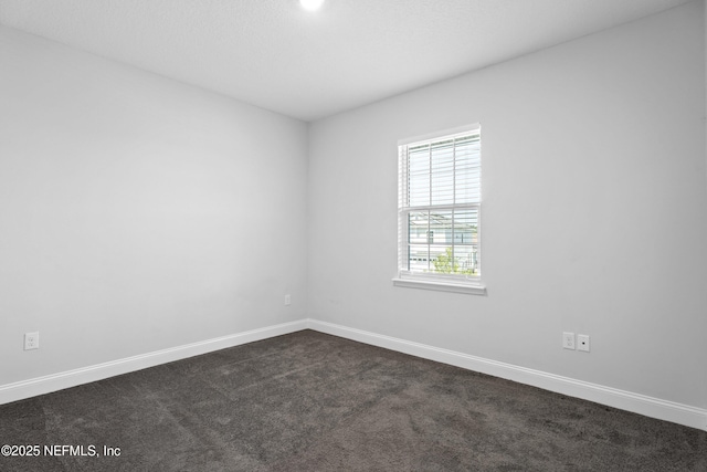 unfurnished room with dark carpet and baseboards