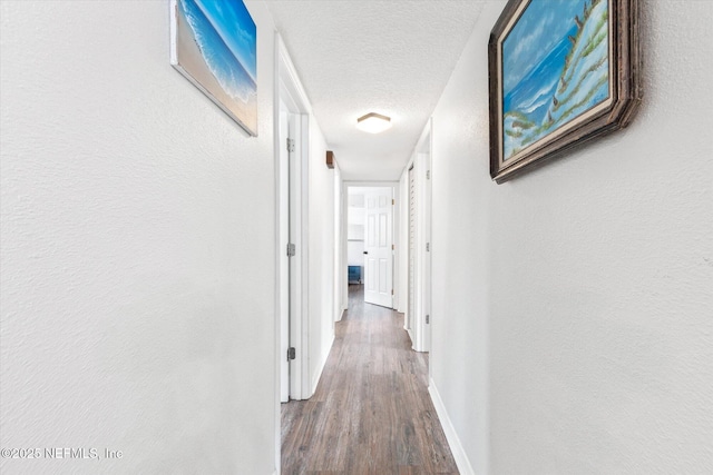 corridor with wood finished floors, a textured ceiling, and baseboards