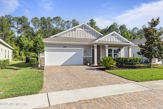 383 Saint Vincent Dr, Saint Augustine, FL 32092 - view of front facade featuring board and batten siding, a front yard, a garage, and stone siding