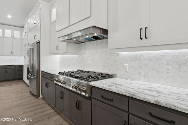97002 Jose Gaspar Way, Yulee, FL 32097 - kitchen with wall chimney range hood, stainless steel appliances, white cabinetry, light stone countertops, and light wood-style floors