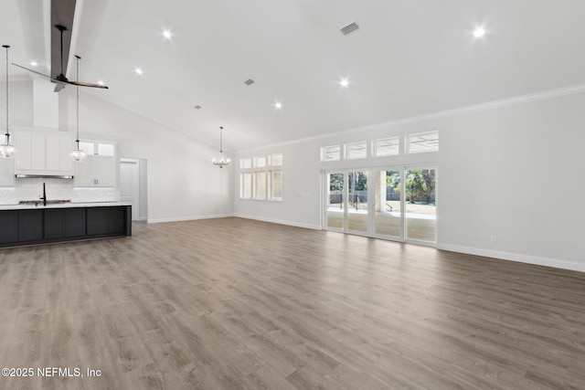 97002 Jose Gaspar Way, Yulee, FL 32097 - unfurnished living room with high vaulted ceiling, a chandelier, baseboards, ornamental molding, and light wood finished floors