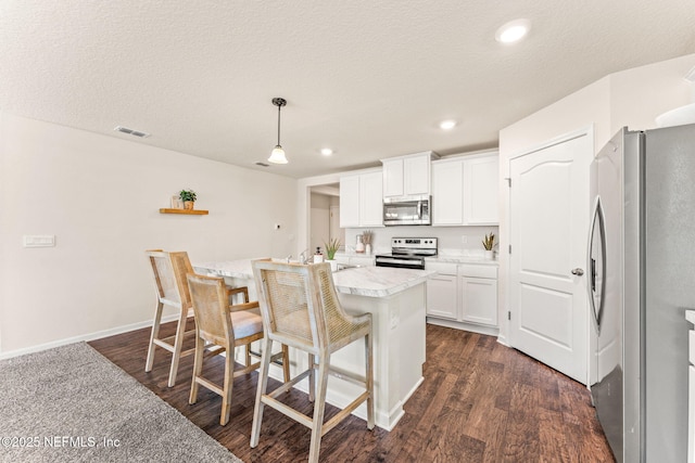 kitchen with appliances with stainless steel finishes, light countertops, white cabinetry, dark wood finished floors, and a breakfast bar