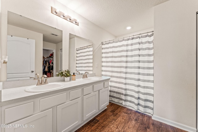 bathroom with wood finished floors, double vanity, a textured ceiling, a walk in closet, and recessed lighting