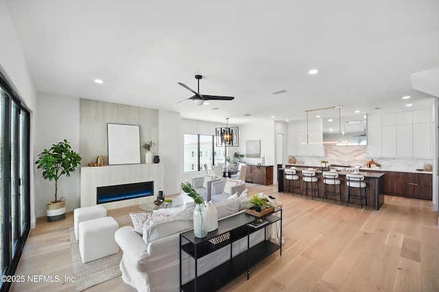 living room with light wood-style floors, ceiling fan, a glass covered fireplace, and recessed lighting