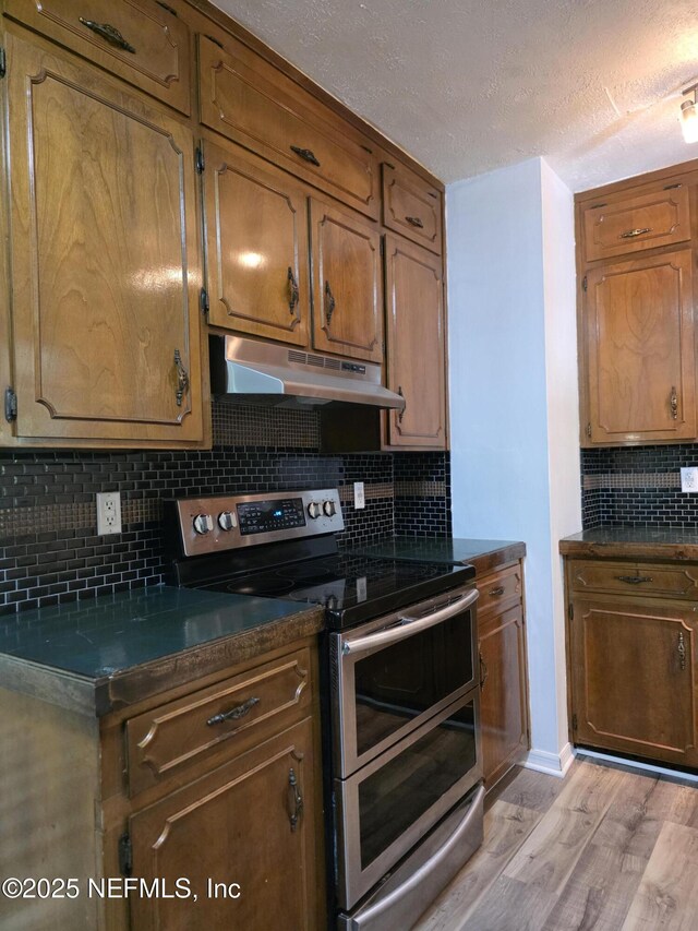 54038 Charles St, Callahan, FL 32011 - kitchen featuring range with two ovens, under cabinet range hood, light wood-style floors, decorative backsplash, and dark countertops