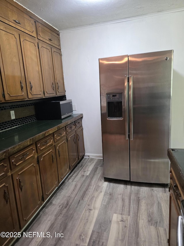 54038 Charles St, Callahan, FL 32011 - kitchen featuring stainless steel fridge, dark countertops, light wood-style flooring, crown molding, and decorative backsplash