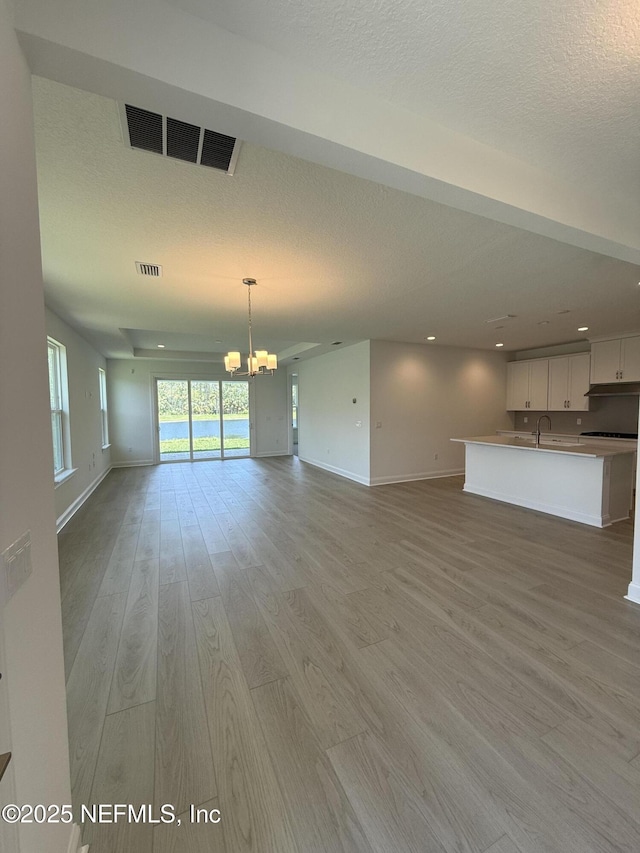 38 Mulberry Rd, Palm Coast, FL 32164 - unfurnished living room with a chandelier, baseboards, light wood-style flooring, a textured ceiling, and a sink