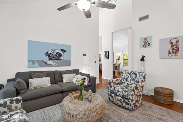 living room featuring wood finished floors, a ceiling fan, baseboards, and a towering ceiling