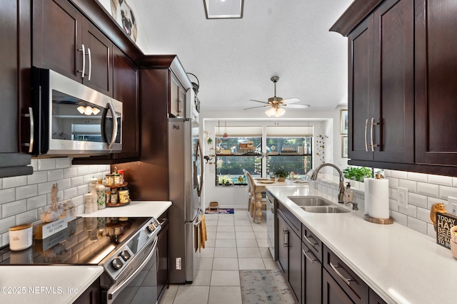 kitchen with a sink, stainless steel appliances, light countertops, dark brown cabinetry, and light tile patterned flooring