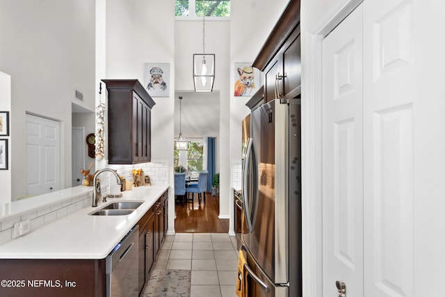 kitchen with appliances with stainless steel finishes, a towering ceiling, a sink, dark brown cabinets, and light countertops
