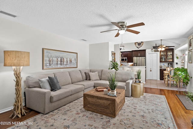 living room with ceiling fan, a textured ceiling, and light wood finished floors