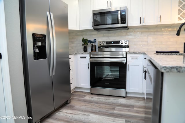1205 Neva St, Jacksonville, FL 32205 - kitchen with appliances with stainless steel finishes, white cabinetry, a sink, light wood finished floors, and tasteful backsplash