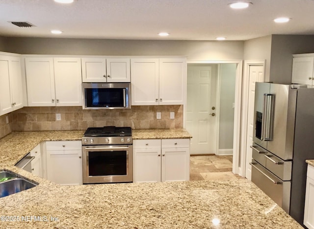 kitchen with appliances with stainless steel finishes, light stone counters, white cabinetry, backsplash, and recessed lighting