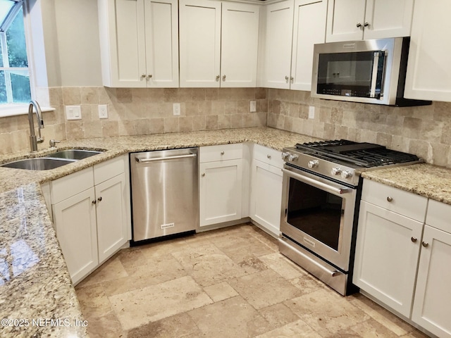 kitchen with appliances with stainless steel finishes, a sink, tasteful backsplash, stone tile floors, and white cabinets