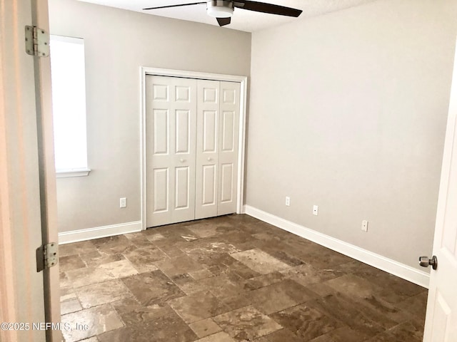 unfurnished bedroom featuring stone finish floors, baseboards, a ceiling fan, and a closet