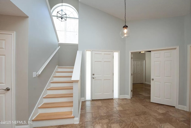 entrance foyer with stone finish floors, high vaulted ceiling, baseboards, and stairs