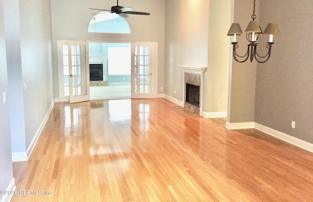 unfurnished living room with a premium fireplace, light wood finished floors, a chandelier, ceiling fan, and a high ceiling
