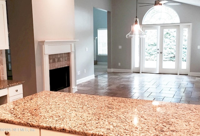 foyer entrance featuring baseboards, a ceiling fan, stone tile flooring, a fireplace, and lofted ceiling