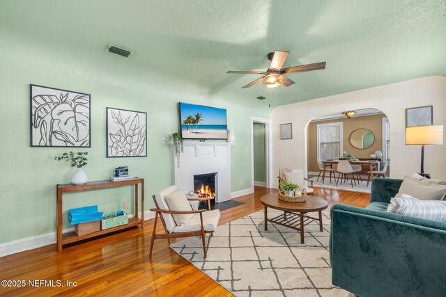 3712 Trask St, Jacksonville, FL 32205 - living room featuring arched walkways, a textured ceiling, ceiling fan, a fireplace with flush hearth, and light wood-style flooring