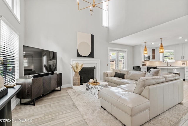 338 Magnolia St, Atlantic Beach, FL 32233 - living room featuring healthy amount of natural light, a chandelier, light wood-style flooring, a towering ceiling, and a fireplace