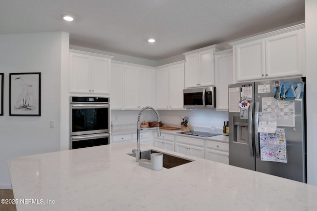 84754 Fall River Pkwy, Fernandina Beach, FL 32034 - kitchen with stainless steel appliances, a sink, white cabinets, light stone countertops, and recessed lighting