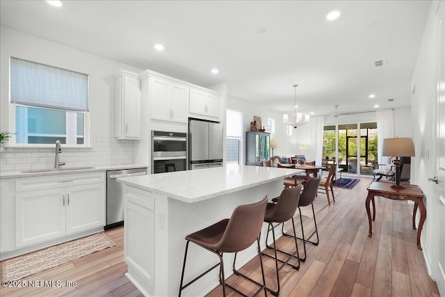 kitchen with appliances with stainless steel finishes, a sink, a kitchen island, light stone countertops, and white cabinetry