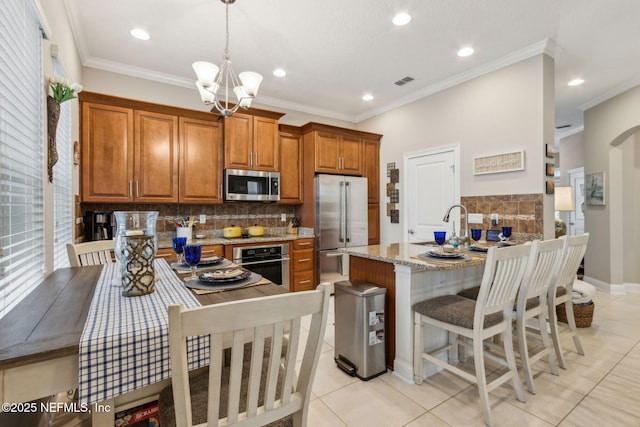 2695 Morning Light Ct, Flagler Beach, FL 32136 - kitchen featuring stainless steel appliances, brown cabinetry, tasteful backsplash, light tile patterned floors, and light stone countertops