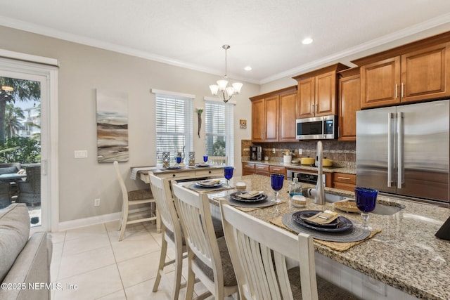 2695 Morning Light Ct, Flagler Beach, FL 32136 - kitchen featuring stainless steel appliances, brown cabinetry, backsplash, light stone counters, and a chandelier