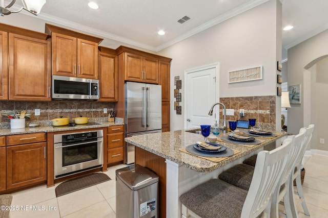 2695 Morning Light Ct, Flagler Beach, FL 32136 - kitchen featuring stainless steel appliances, light tile patterned floors, brown cabinetry, light stone counters, and a sink