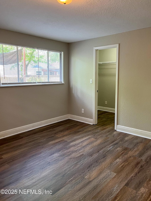 4522 Kingsbury St, Jacksonville, FL 32205 - unfurnished bedroom featuring dark wood-style flooring, baseboards, a closet, a textured ceiling, and a walk in closet