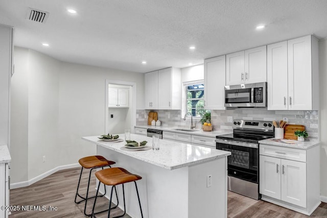10859 Windy Gale Dr W, Jacksonville, FL 32218 - kitchen with stainless steel appliances, a sink, a breakfast bar area, backsplash, and light wood-style floors