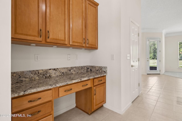 3384 Olympic Dr, Green Cove Springs, FL 32043 - kitchen featuring crown molding, light stone counters, brown cabinets, light tile patterned flooring, and baseboards