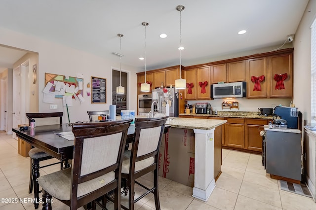 1071 Wetland Ridge Cir, Middleburg, FL 32068 - kitchen featuring appliances with stainless steel finishes, light tile patterned floors, a center island with sink, brown cabinets, and recessed lighting