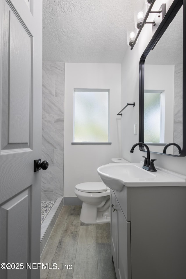 2210 Lamee Ave, Jacksonville, FL 32207 - full bath with a textured ceiling, toilet, vanity, a tile shower, and wood finished floors