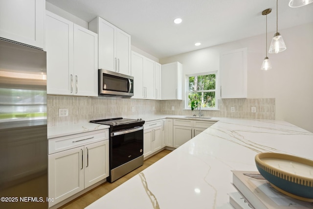 kitchen with appliances with stainless steel finishes, a sink, tasteful backsplash, pendant lighting, and white cabinetry