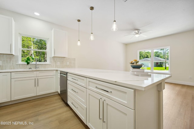 kitchen featuring stainless steel dishwasher, a peninsula, a sink, ceiling fan, and backsplash