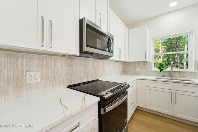 kitchen featuring stainless steel microwave, electric range, a sink, white cabinets, and backsplash